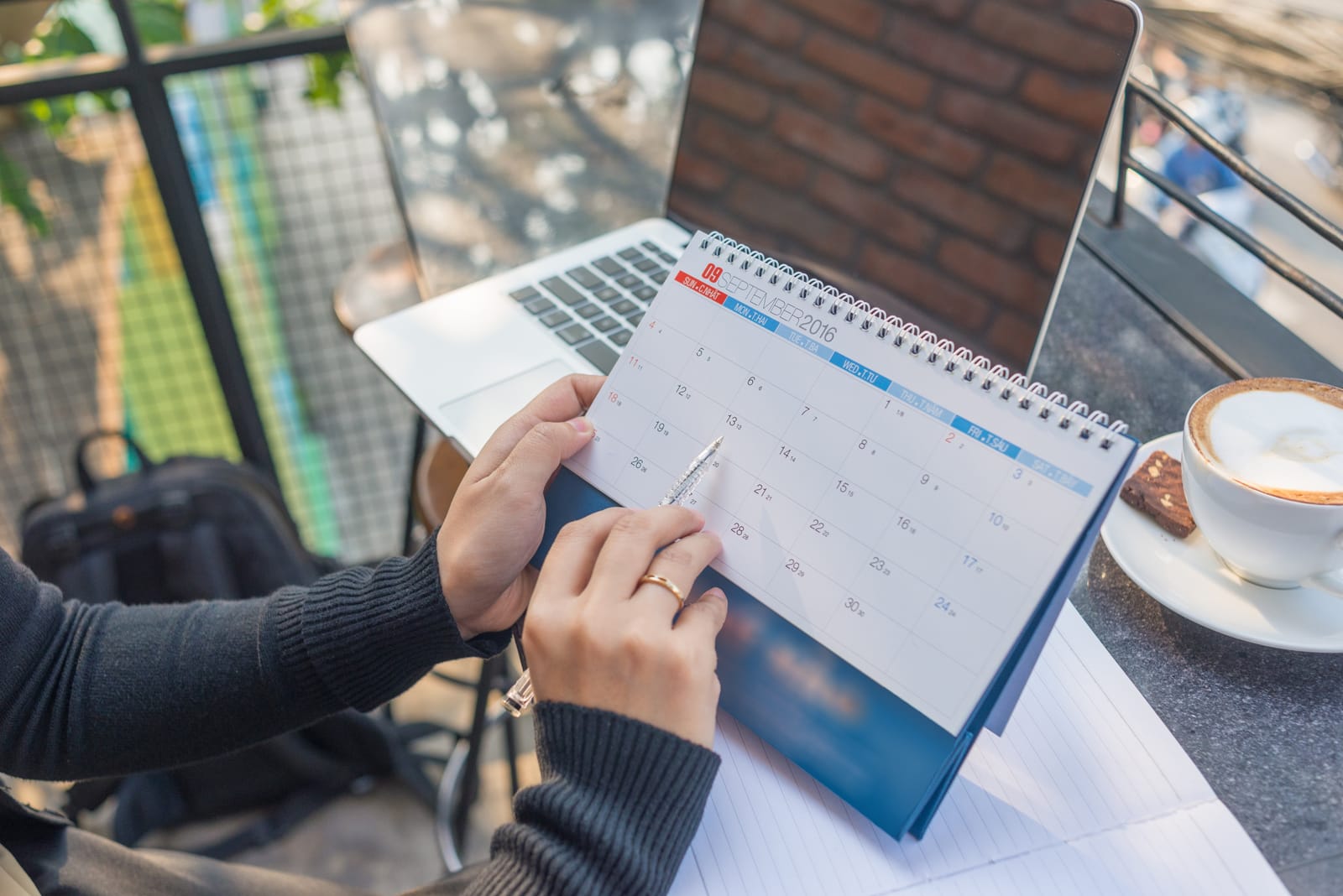 Handen met een maandplanner naast een laptop
