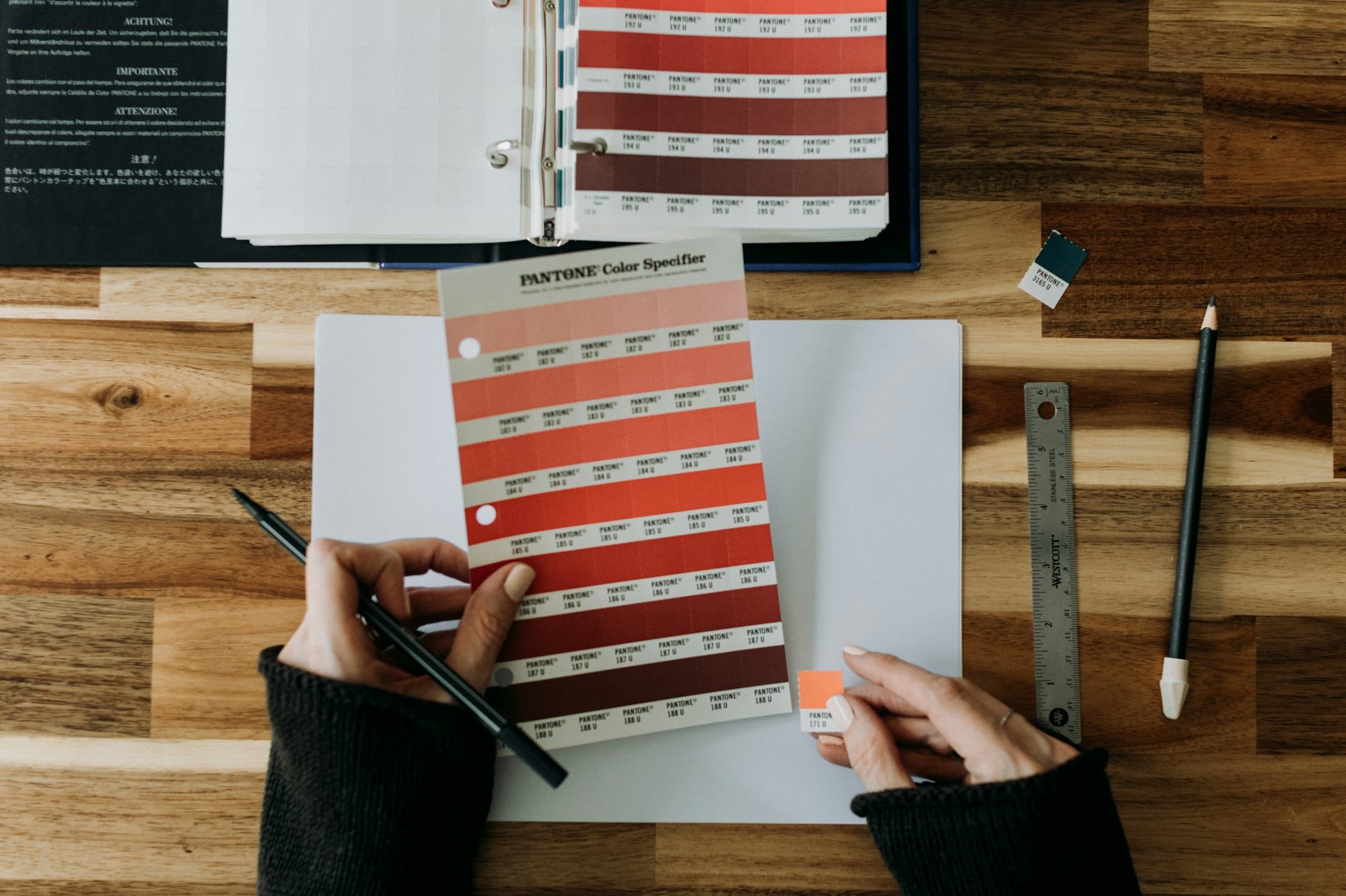 Ontwerper kiest kleuren uit een Pantone-waaier aan een houten bureau