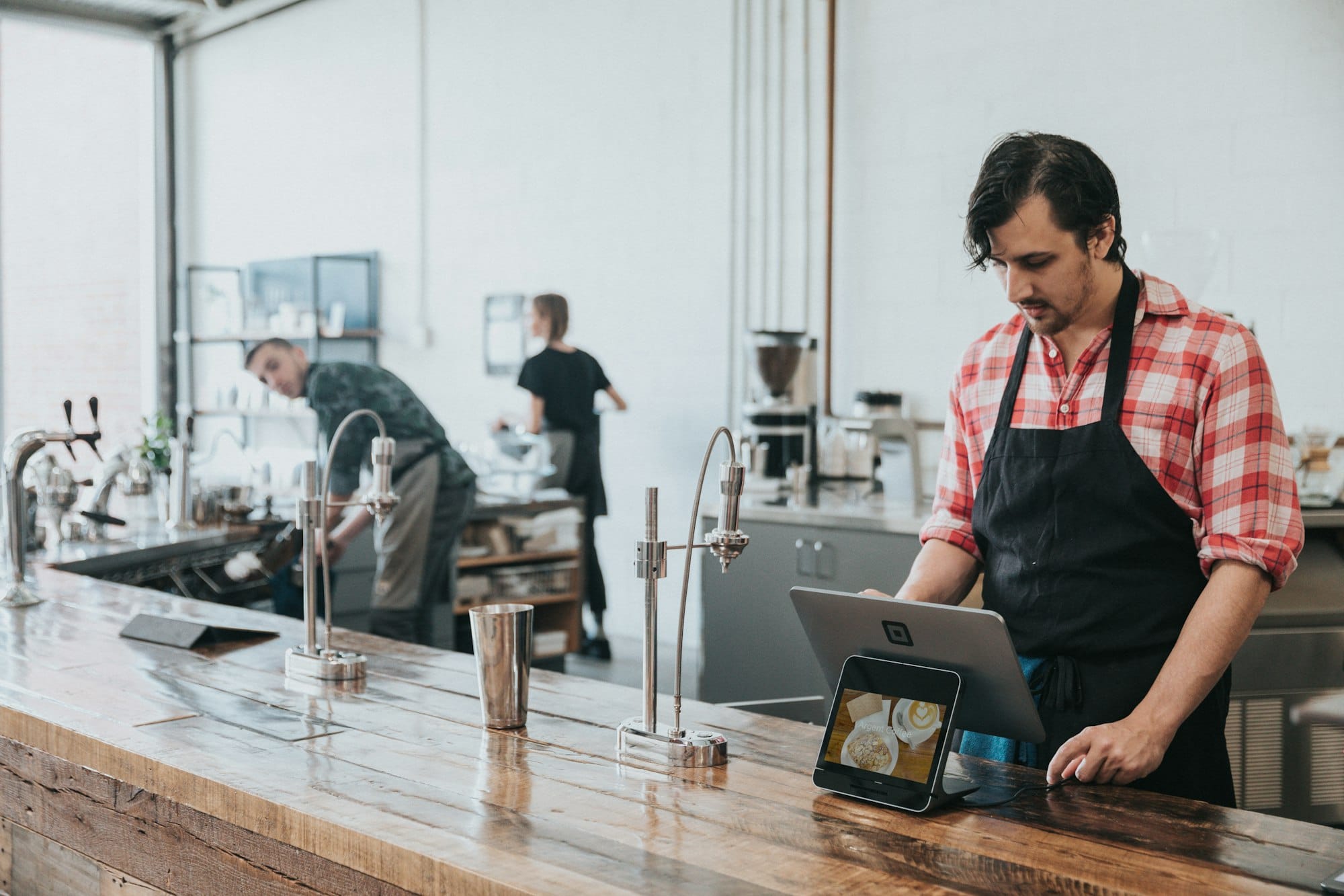 Barista achter houten toonbank bedient een kassa op tablet in koffiebar