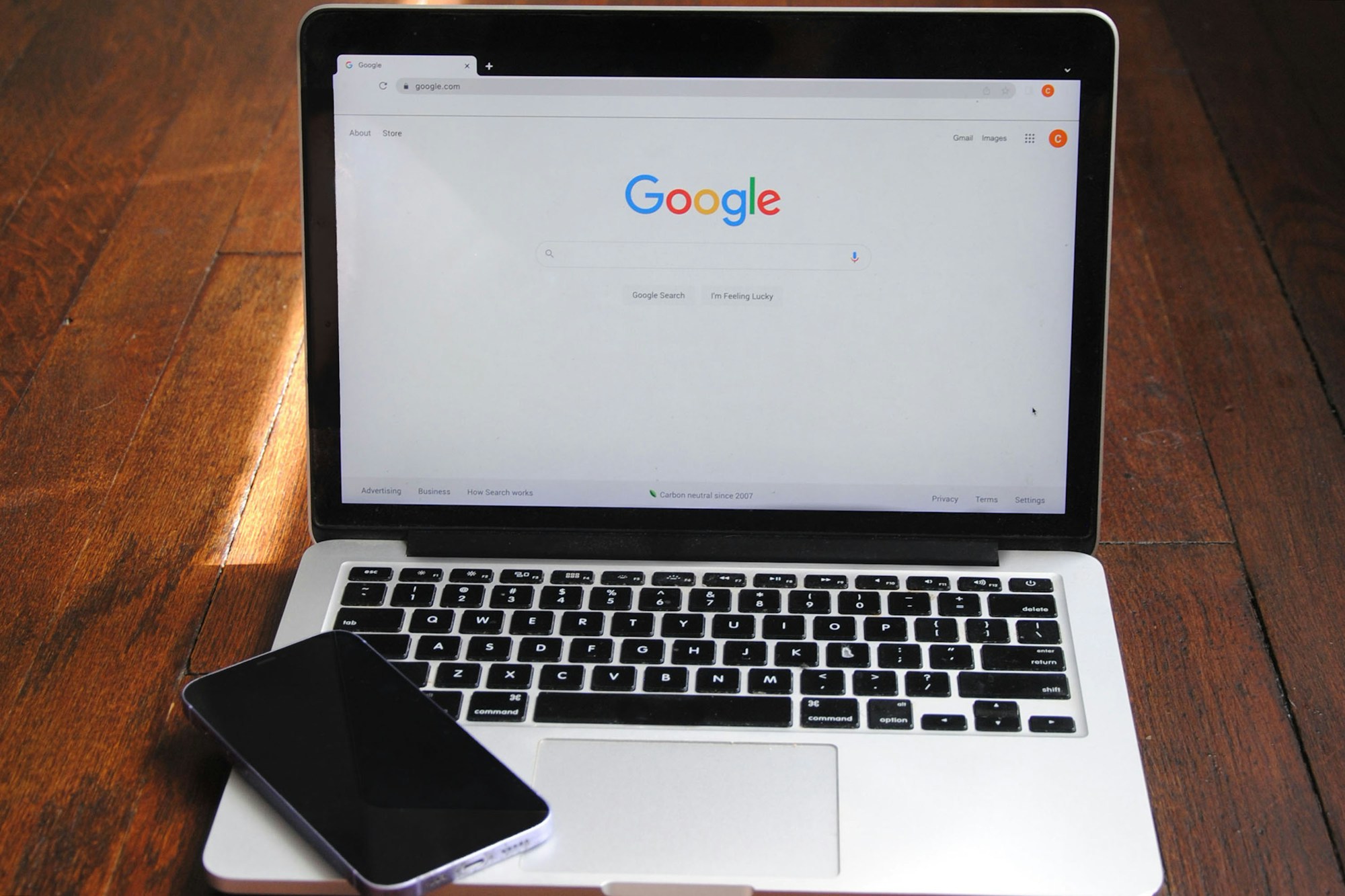 Laptop met de Google-zoekpagina en een telefoon op een houten tafel