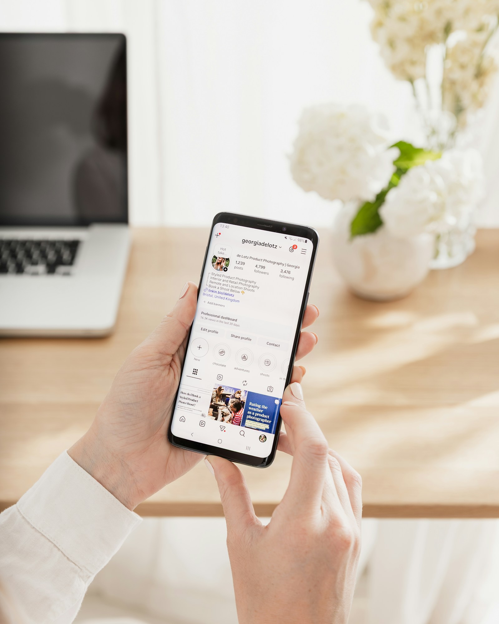 Handen bekijken een Instagram-profiel op een telefoon aan een licht bureau